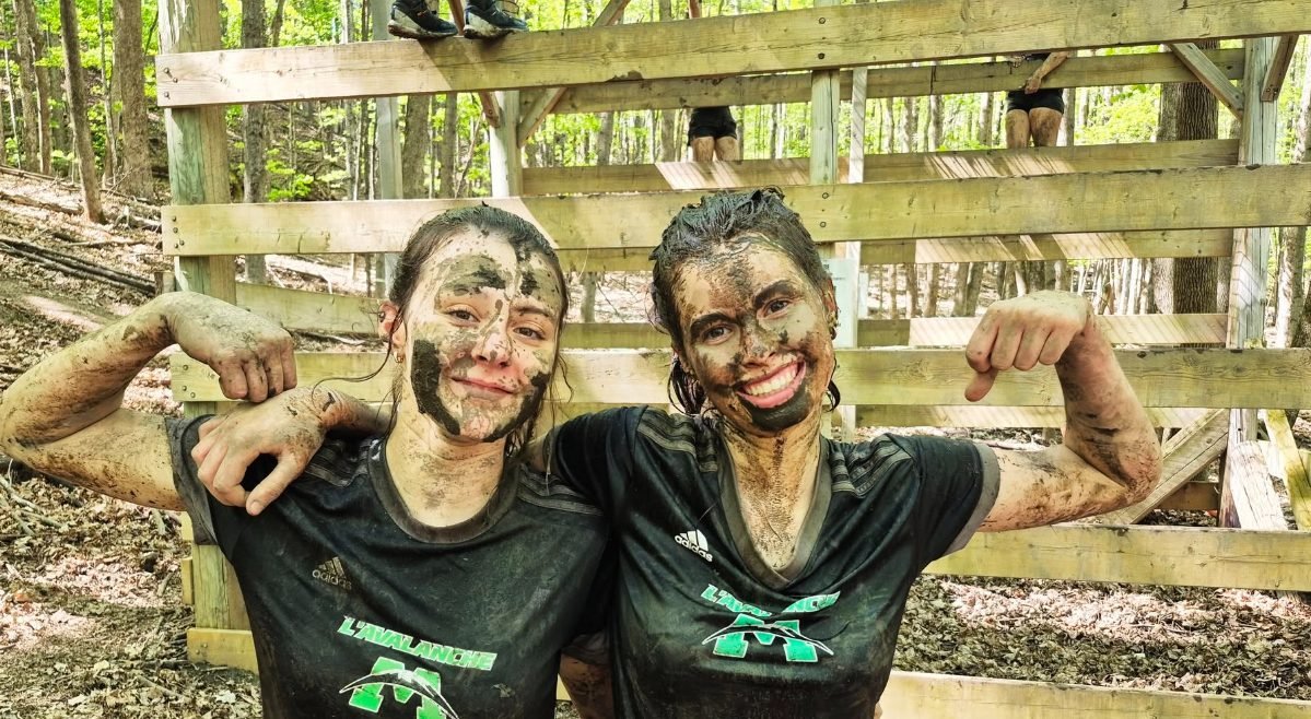 Deux jeunes couvertes de boue, souriantes, fléchissant les bras après le parcours